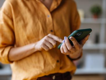 A person in a button-down shirt scrolls on a smartphone.