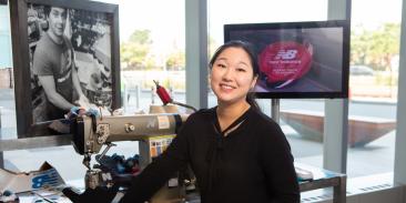 A former Climate Corps fellow inside a brightly lit building, with a screen displaying the New Balance logo.