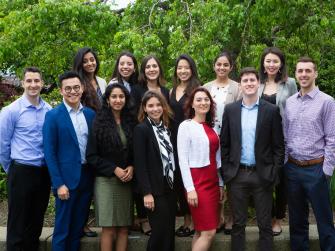 13 EDF Climate Corps fellows outdoors, with many trees in the background. They are smiling and in formal attire.