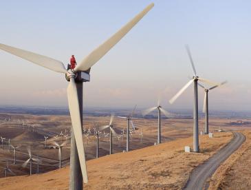 High-angle view of a worker atop a wind turbine in a rural setting.