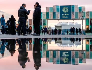 People chat outside a building displaying a teal COP29 banner.